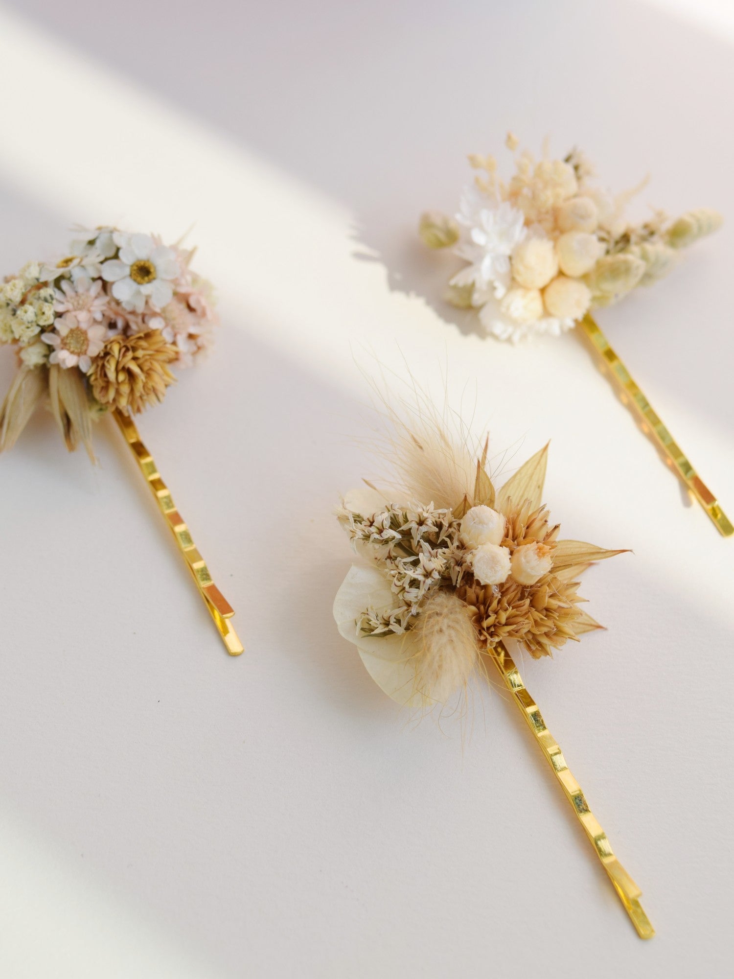 Drie samen passende goudkleurige haarschuivers met droogbloemen op bevestigd in een moderne stijl, als haaraccessoires voor bruiden, beige, witte en zandkleurige tinten 