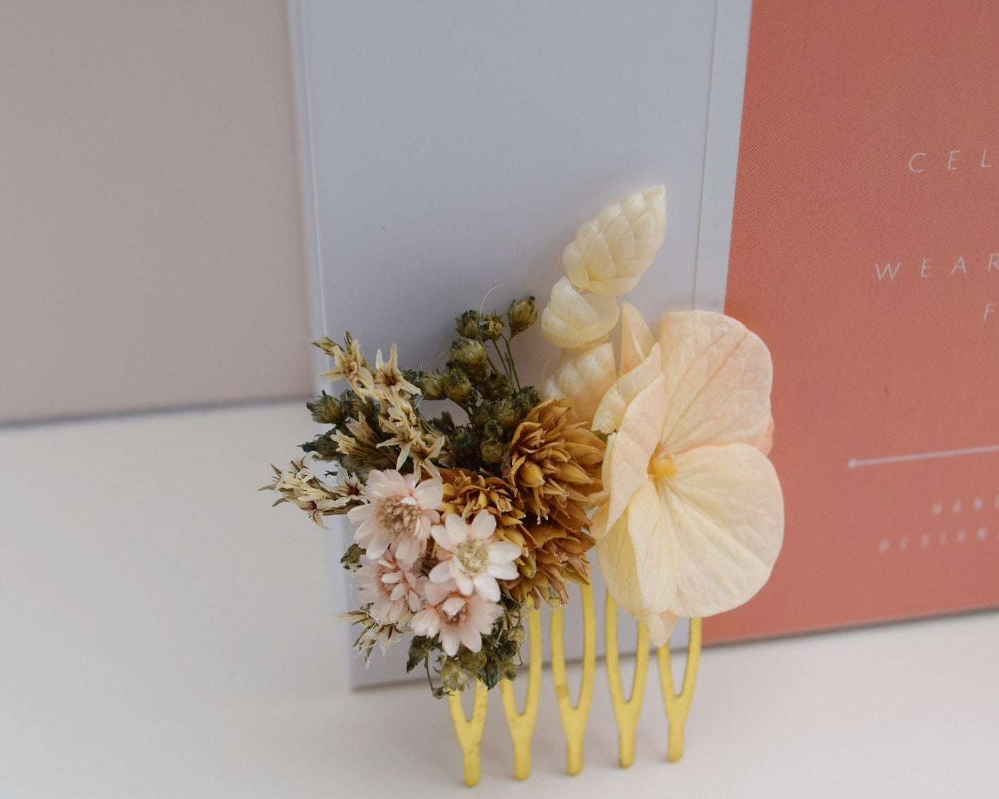 Mini gouden haarkam die gemaakt is van droogbloemen zoals perzikkleurige hortensia, groene broom, nude glixia en bruine hillsflowers