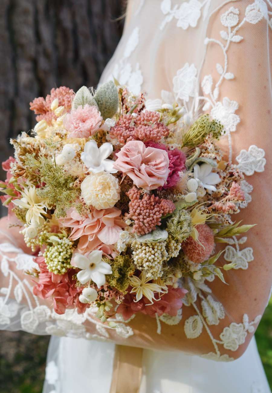 romantisch roos rond bruidsboeket gemaakt van droogbloemen met tuinrozen, anjers, hortensia en witte jasmine. Vastgehouden door een bruid