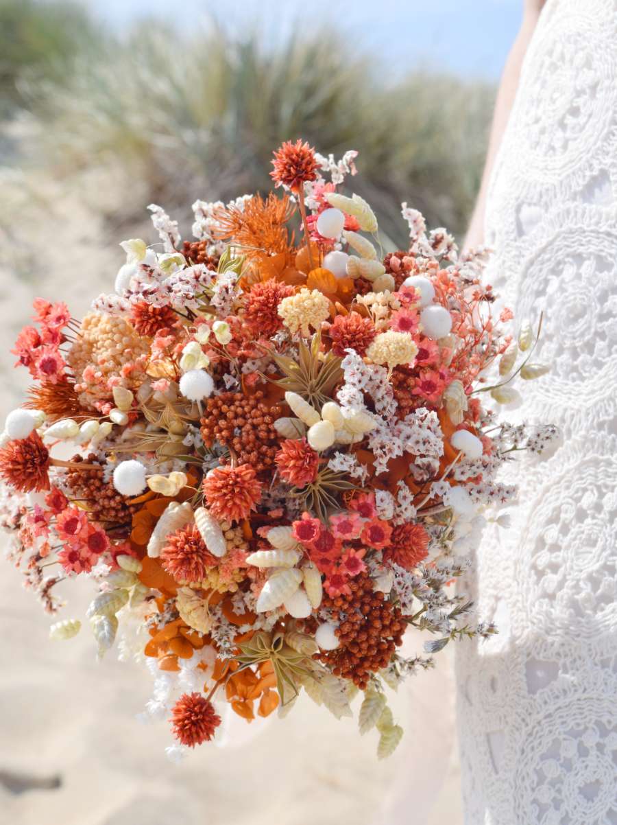 Close-up van een rond en compact trouwboeket van droogbloemen met oranje rijstbloemen, oranje hortensia, nigella, witte breeza, tatarica en oranje glixia bloemen