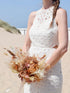 Bruid staat in de duinen en draagt een modern trouwboeket van droogbloemen. Het droogboeket heeft een boho vibe en bevat pampas, strelitzia, hortensia en gepreserveerde rozen.