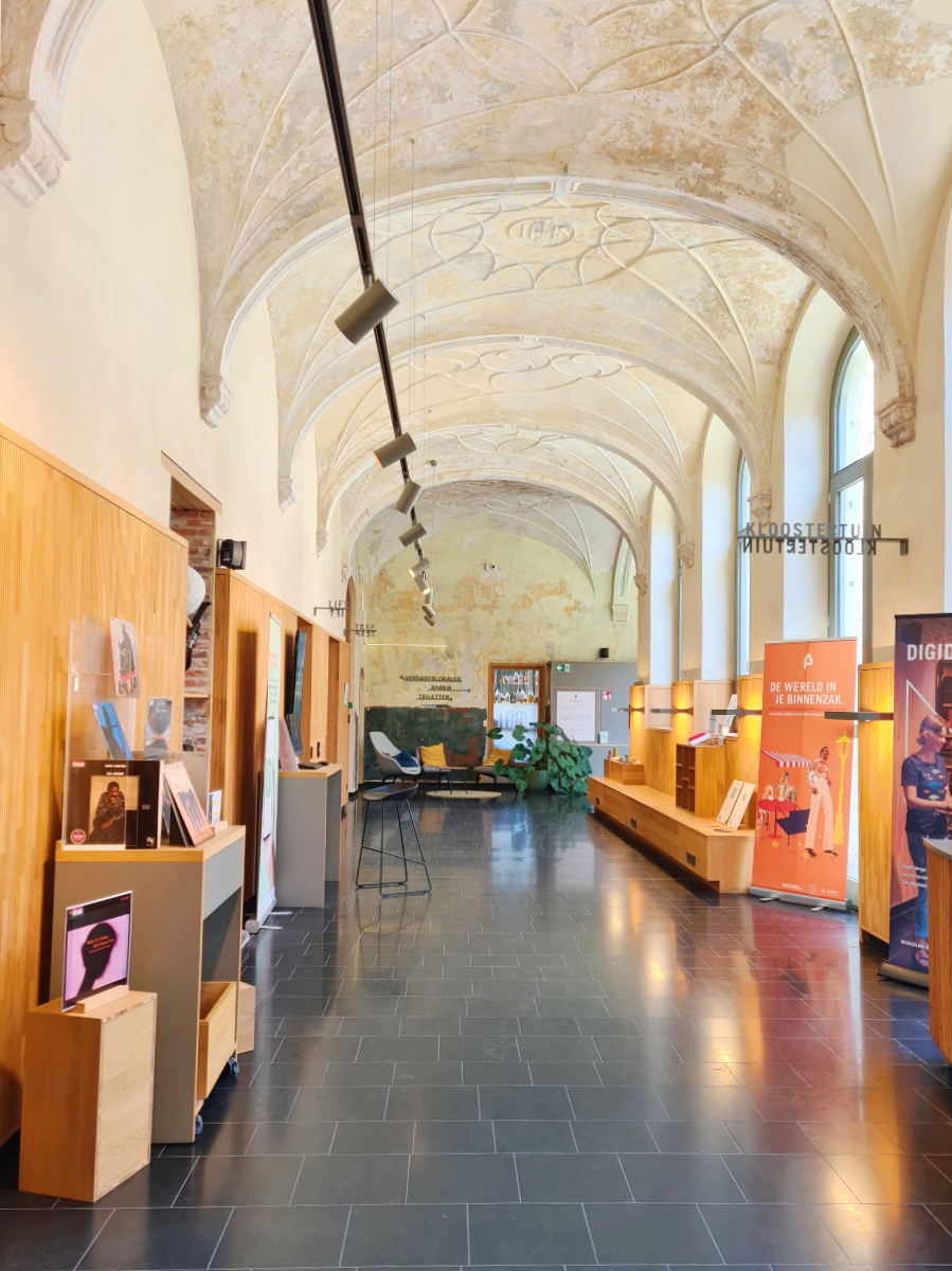 Gangpad van bibliotheek van Mechelen met oude gewelven en een moderne stenen vloer, in de verte een knusse zithoek