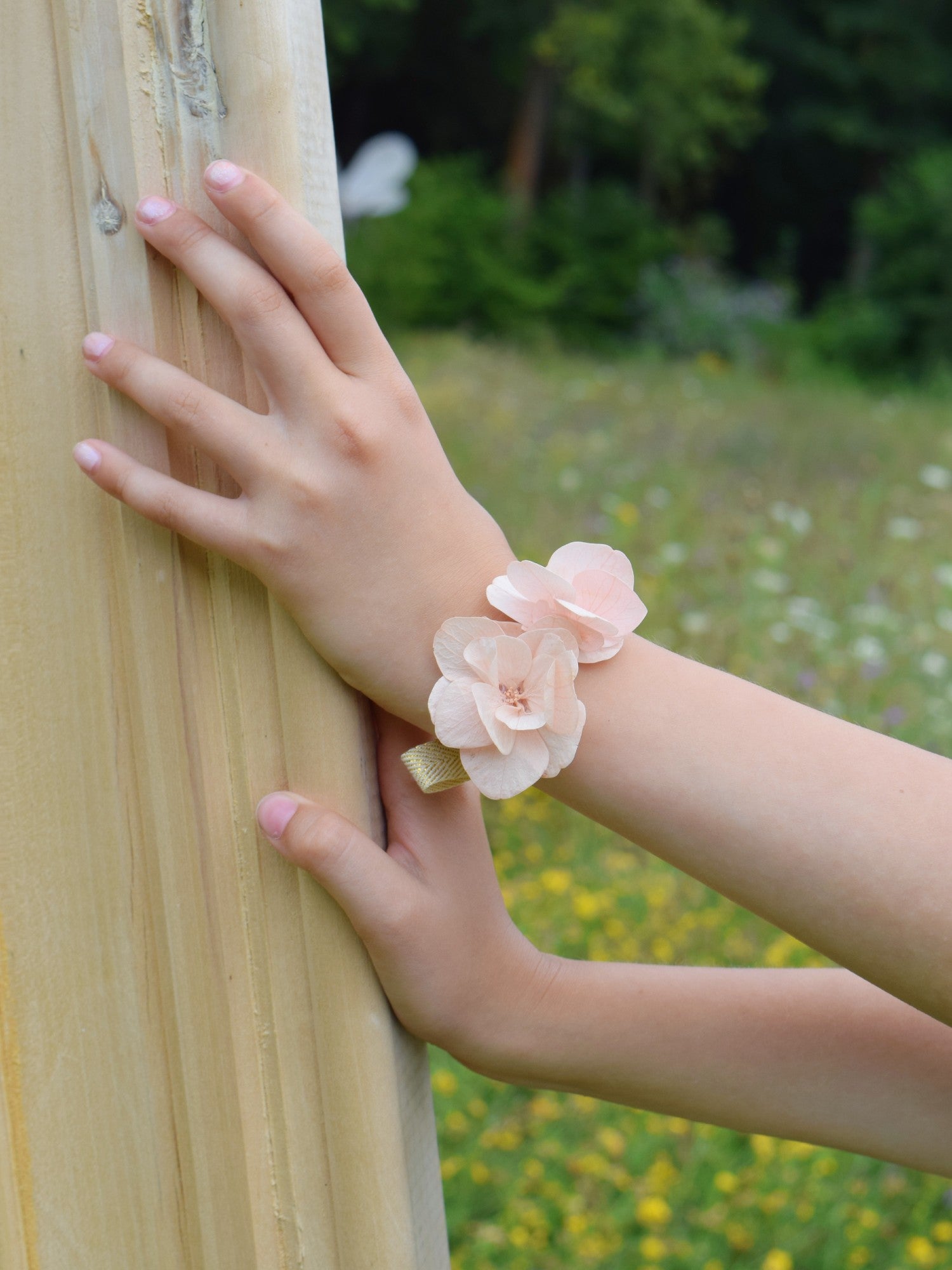 Kinderhand met een armband die met de hand werd gemaakt van droogbloemen en volledig bestaat uit zachtroze hortensiablaadjes