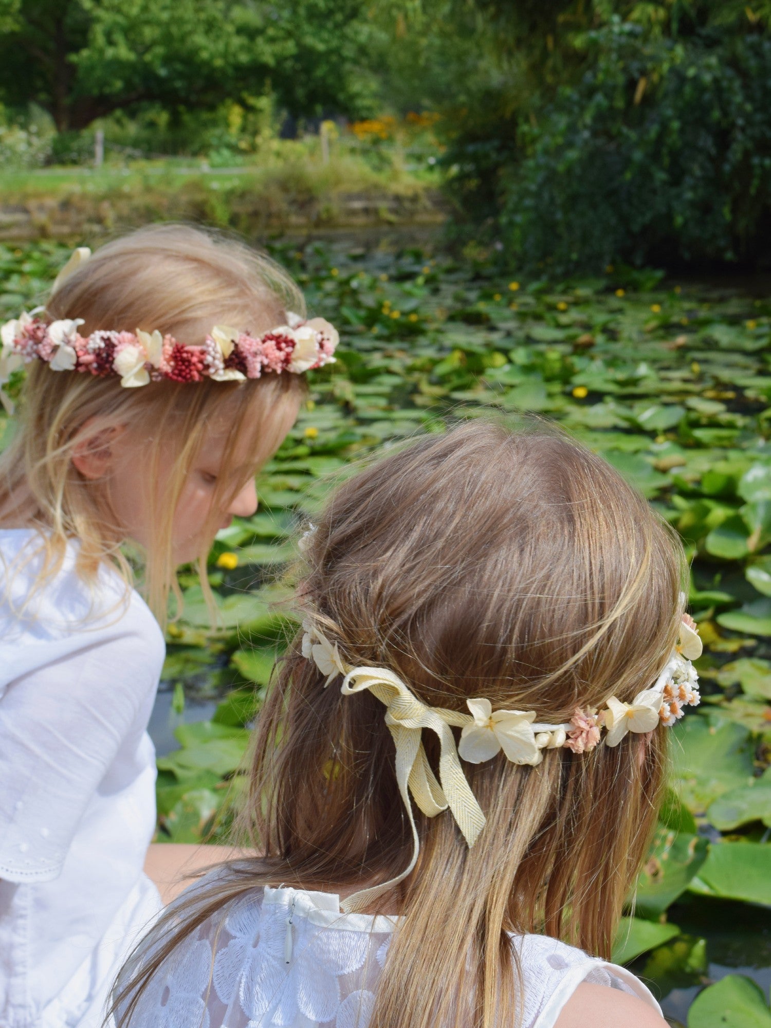 Twee blonde meisjes van zeven jaar met wit communiekleedje en een handgemaakte bloemenkroon in roos en zalm