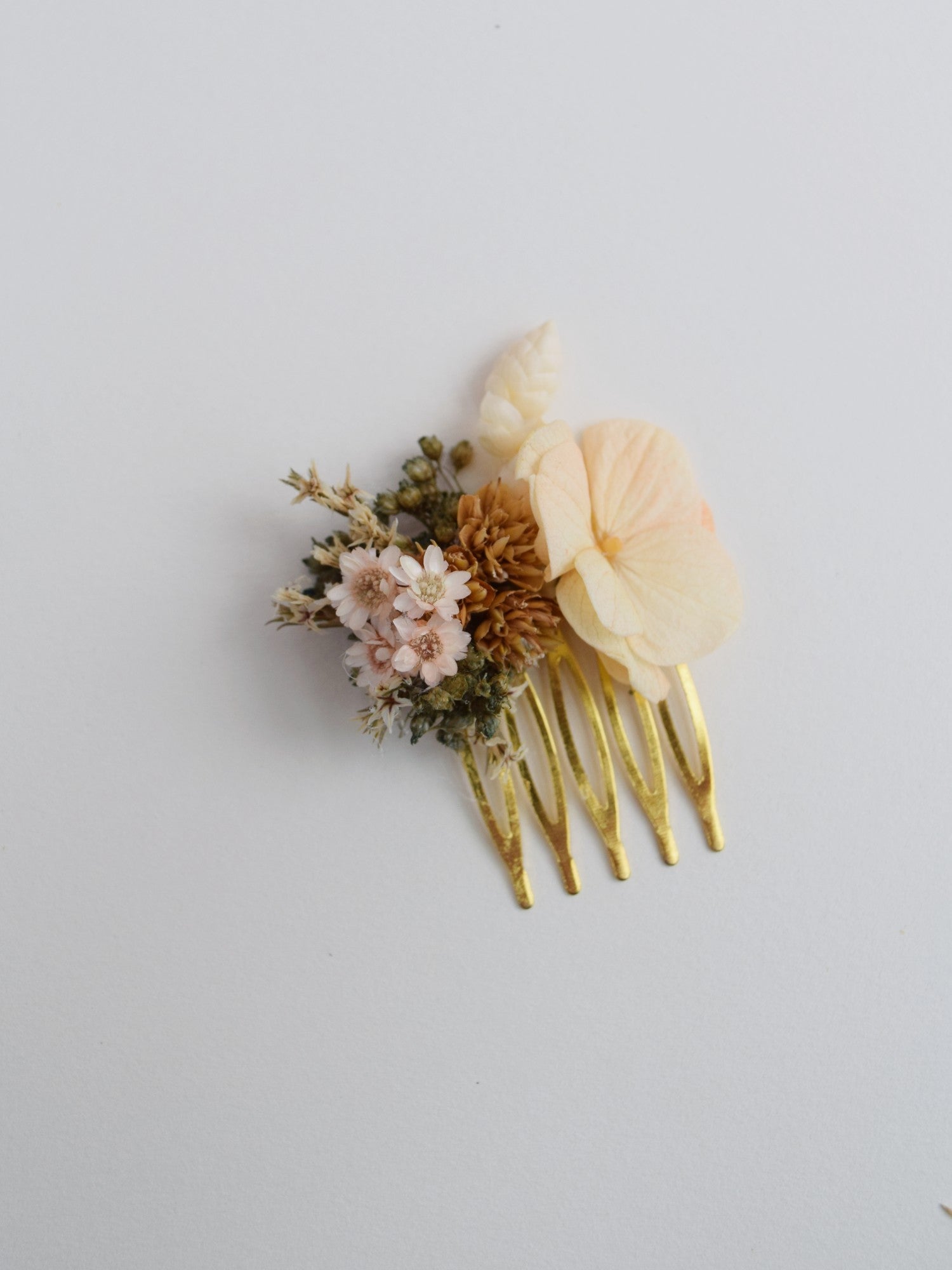 kleine gouden haarkam met bovenaan decoratie van droogbloemen zoals perzikkleurige hortensia, groene broom en witte breeza