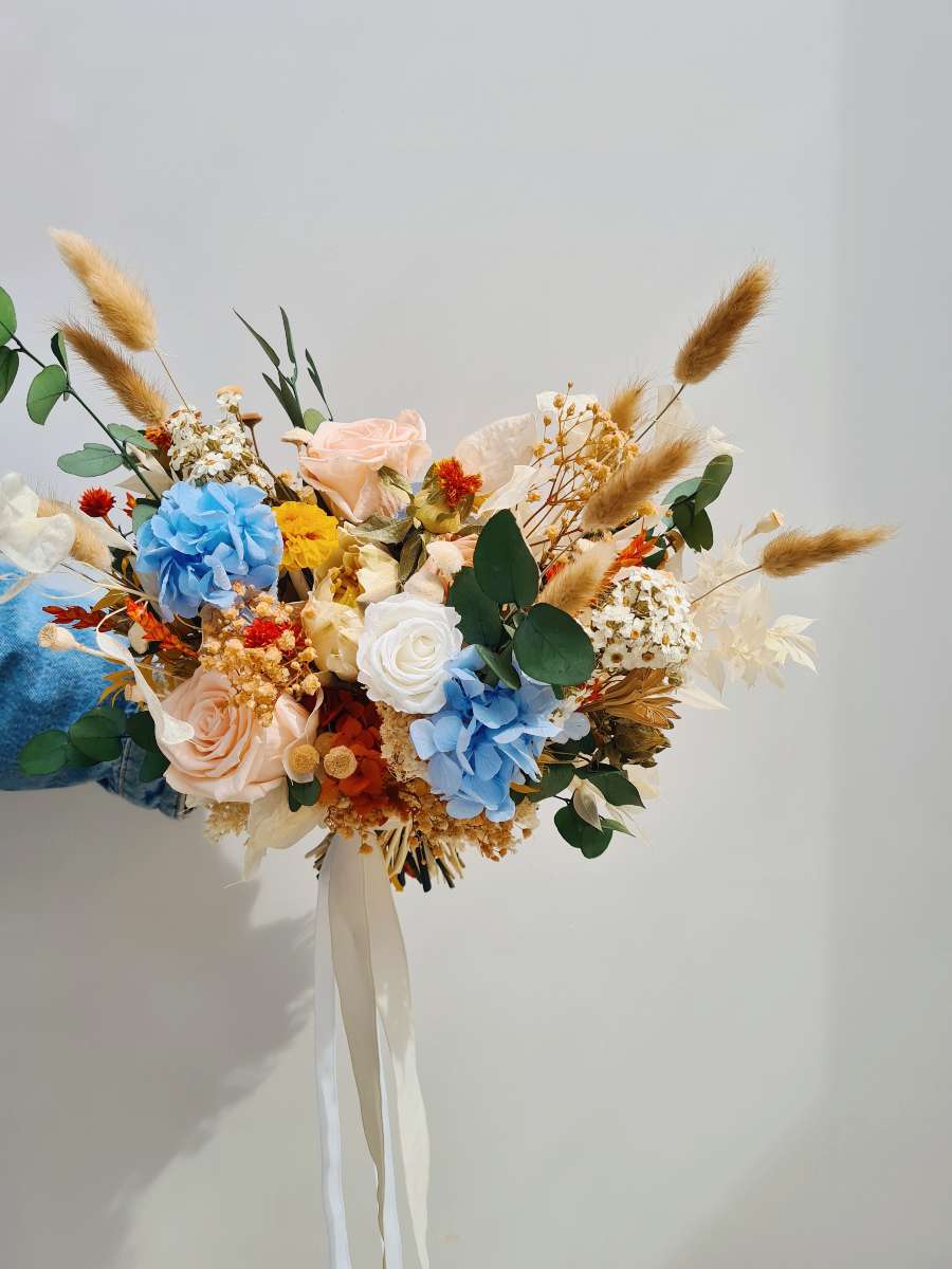 Een kleurrijk bruidsboeket van droogbloemen met blauwe hortensia, groene eucalyptus en oranje, gele tinten