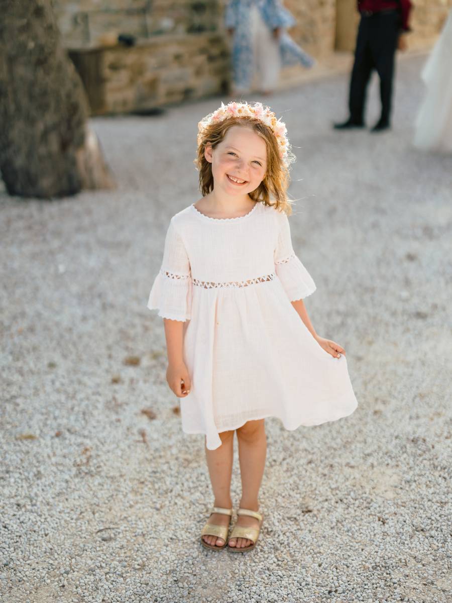 Kind met een zwierige witte kanten jurk en een fragiele bloemenkroon in het haar met roze en witte droogbloemen