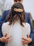 Foto van een bruidskoppel waarbij de achterkant van de bruid zichtbaar is en je een handgemaakte bloemenspeld van droogbloemen kan zien in witte, oranje en terracotta tinten
