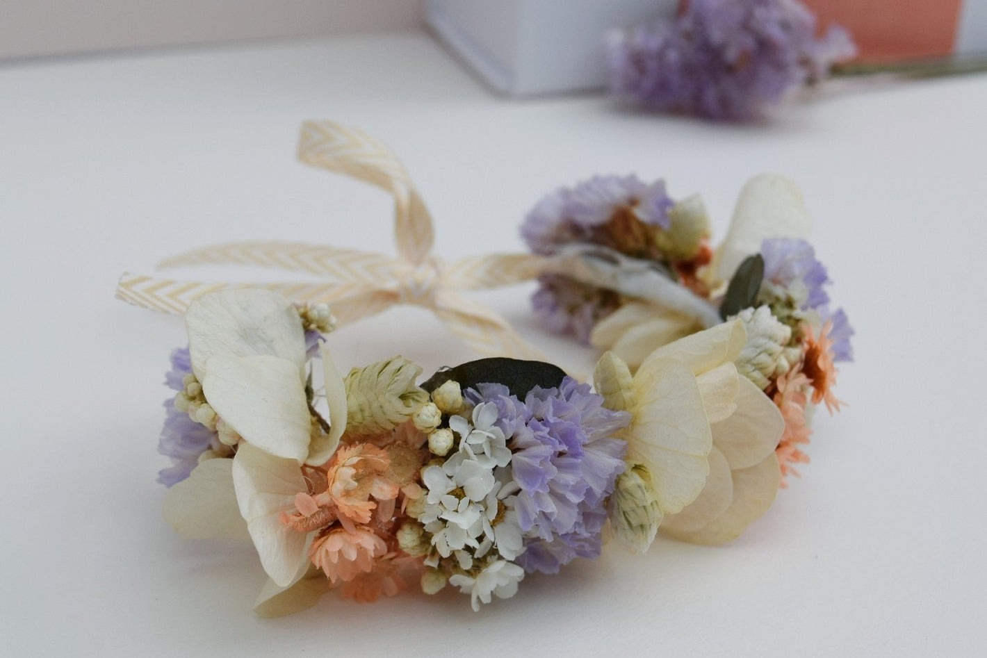 Handgemaakte armband van droogbloemen in pasteltinten waaronder crèmekleurige hortensia, mauve statice, groene breeza en oranje glixia bloemetjes. Dun lint bevestigd om de armband vast te knopen rond de pols