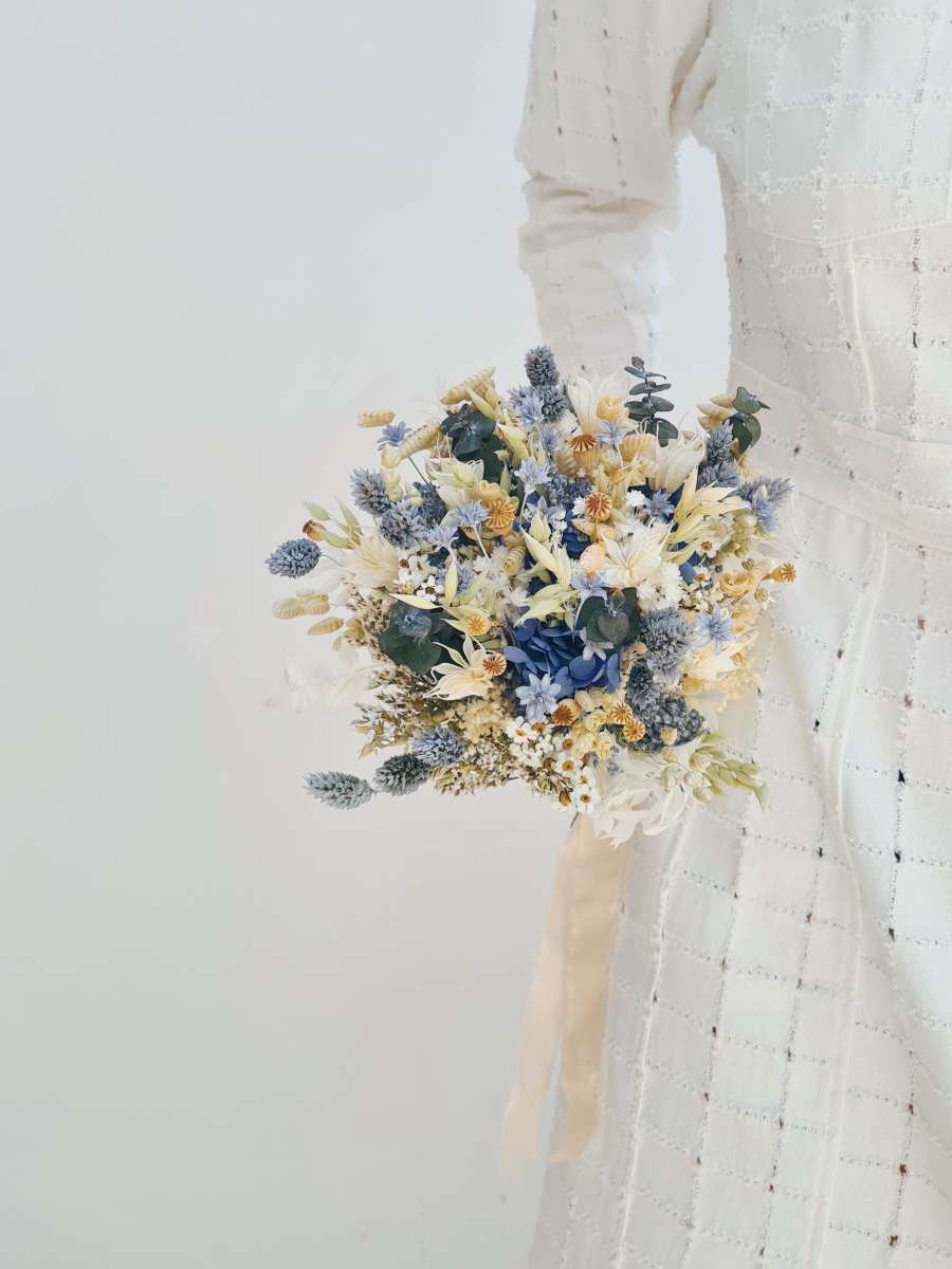 Close-up van een klein bruidsboeket van droogbloemen dat wordt vastgehouden en werd gemaakt van blauwe hortensia, papavers, havers en phalaris.