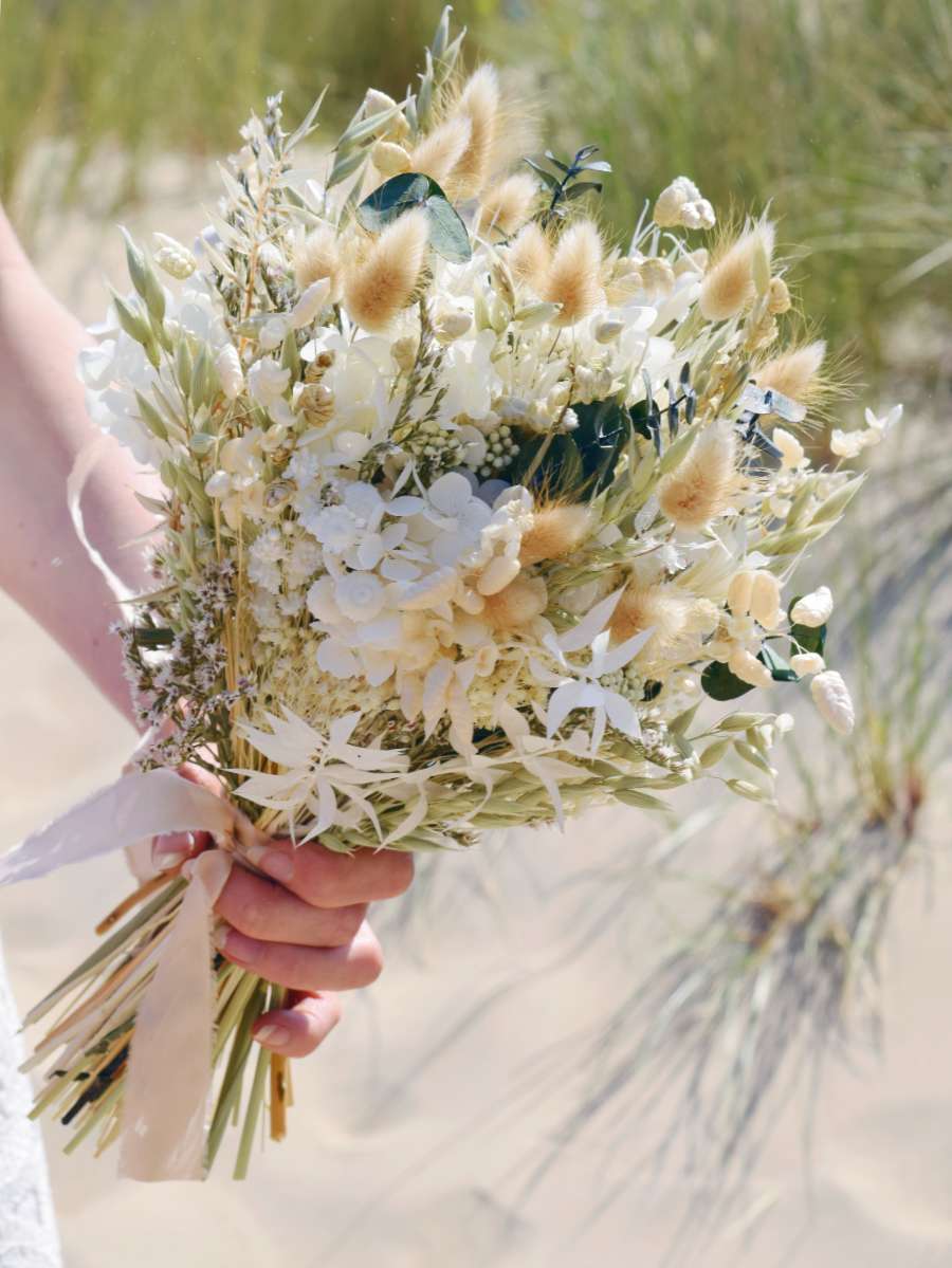 close-up van een klein trouwboeket van droogbloemen met champagnekleurig lint en gemaakt van witte hortensia, groene eucalyptus en haver