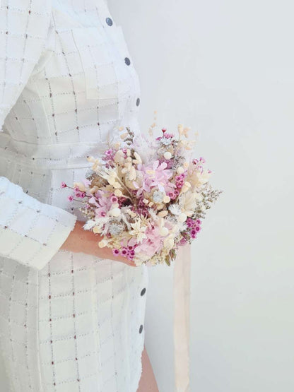 Model poseert met een klein bruidsboeket van droogbloemen met lila hortensia, paarse glixia, witte papaver en nigella met een lang lint