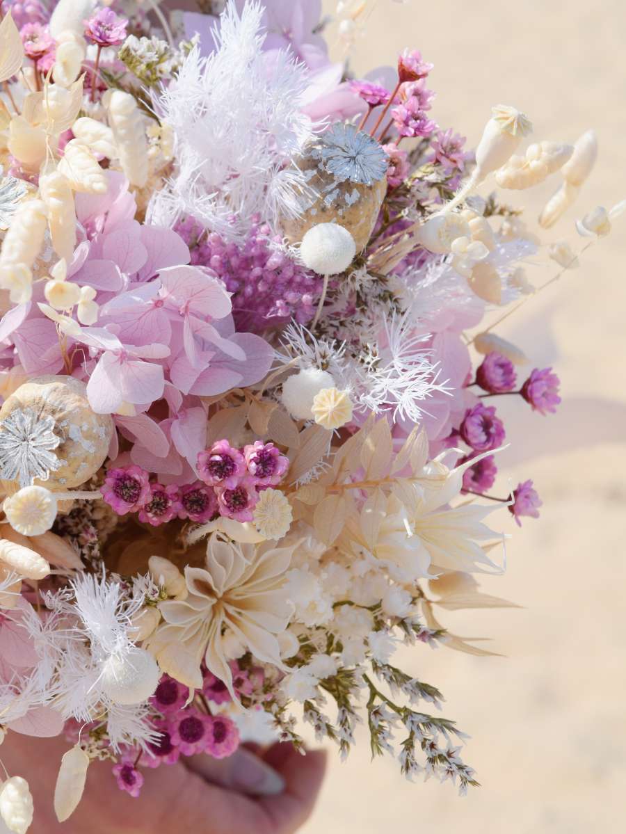 Close-up van een trouwboeket met droogbloemen waarbij je lila hortensia, witte botao, papavers en ruscus ziet