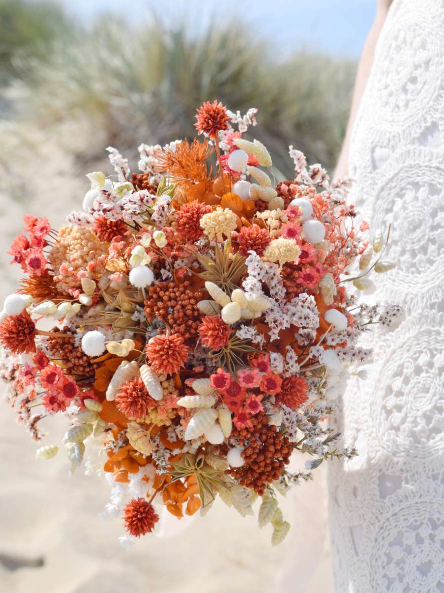 Close-up van een rond en compact trouwboeket van droogbloemen met oranje rijstbloemen, oranje hortensia, nigella, witte breeza, tatarica en oranje glixia  bloemen