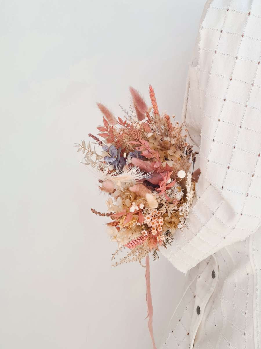 Close-up van een modern bruidsboeket van droogbloemen met een romantische uitstraling en zachtroze, oranje en witte tinten.