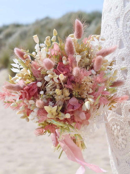 Close-up van een rond en compact bruidsboeket van droogbloemen met een romantische uitstraling. Het droogboeket bevat roze hortensia, bunny tails, witte broom, groene haver en nog zoveel meer.