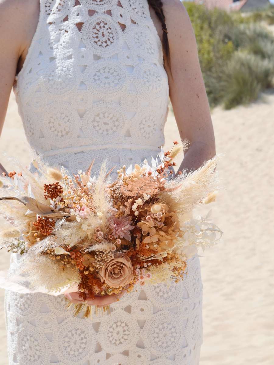 Close-up van een modern en boho bruidsboeket in mokka en terracotta tinten met pampas, gepreserveerde rozen en varens