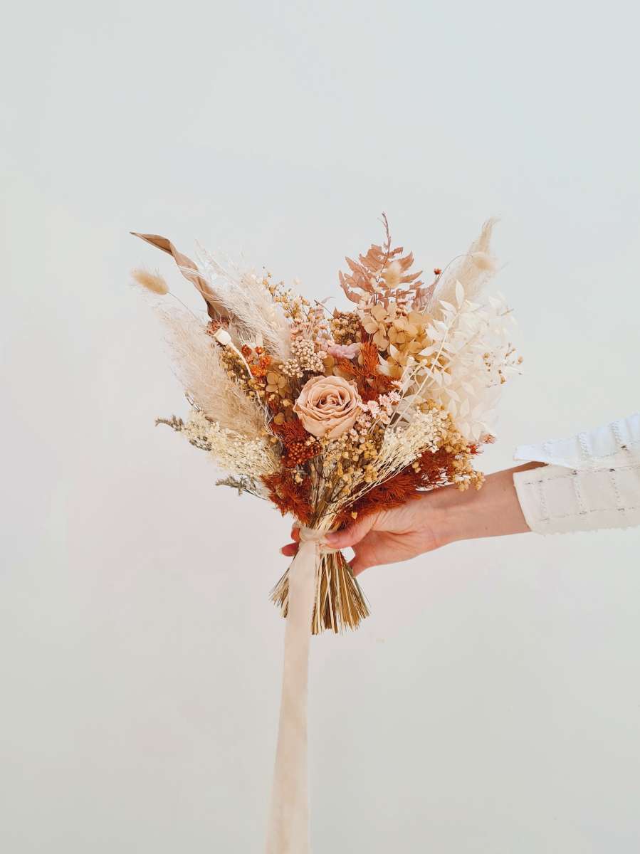Bruidsboeket van droogbloemen in terracotta tinten met beige pampas en een lang lint