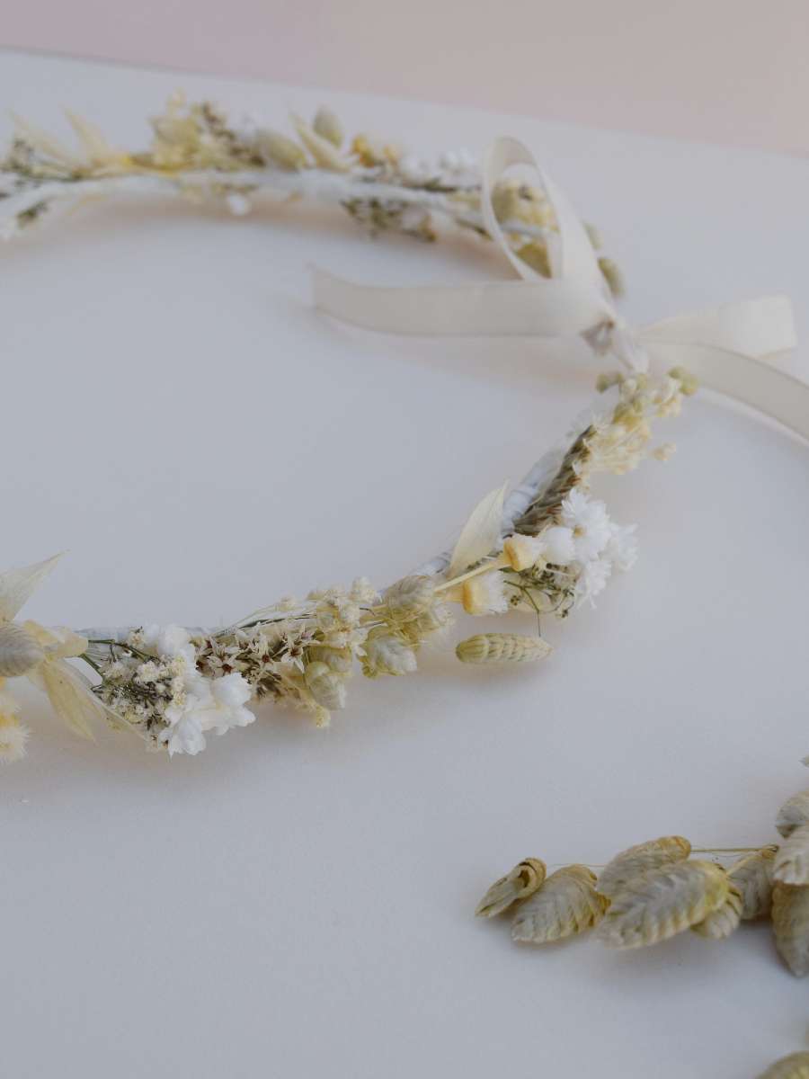 detailfoto van een bloemenkroontje in witte en zachtgroene tinten voor een communiefeest dat neerligt en werd afgewerkt met witte linten