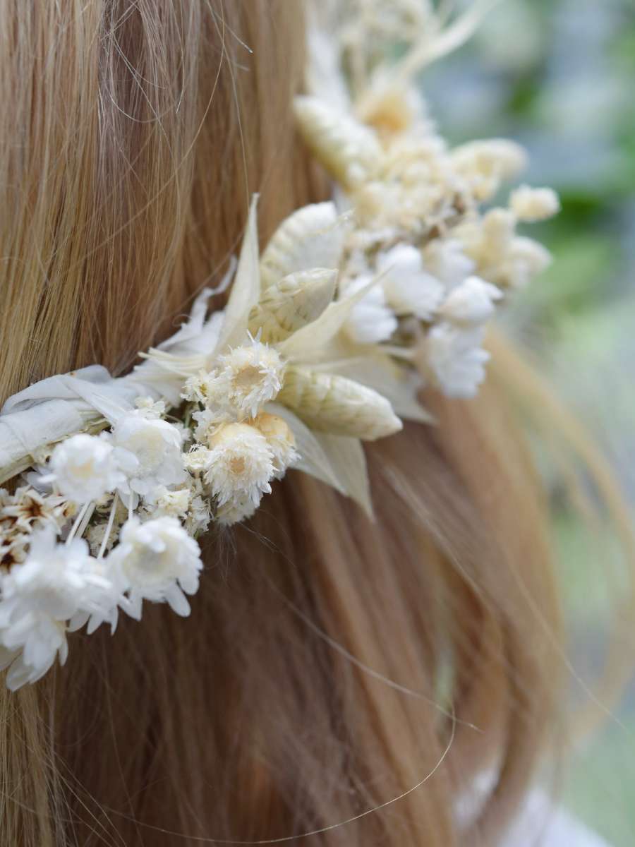 detailfoto van een bloemenkroon die werd samengesteld in witte en zachtgroene droogbloemen, gedragen door een blond meisje